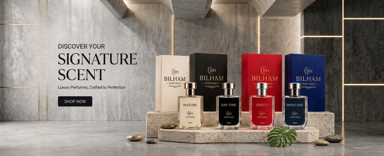 A promotional display of four Billham perfume bottles and their matching boxes on a stone pedestal, set against a modern gray marble wall with gold lines. The bottles are in cream, black, red, and blue glass, with the corresponding Billham boxes in cream, black, red, and blue.